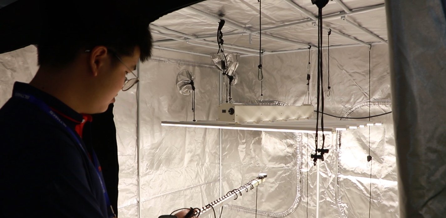 Engineer taking a quantum-sensor reading under an LED fixture in a test tent